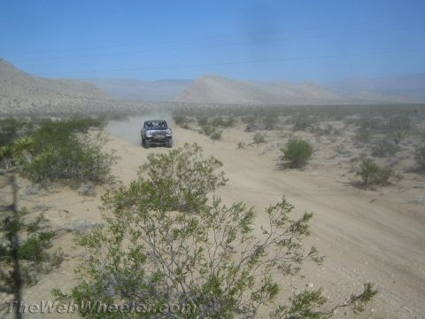 1990 Ford Bronco - light-colored truck raises dust on a sandy desert road with low mountains beyond.