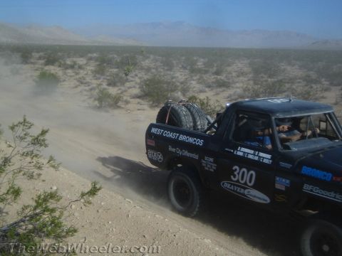 1990 Ford Bronco - black early Ford Bronco race rig with spare tires and West Coast Broncos number 300 livery speeds across the desert.