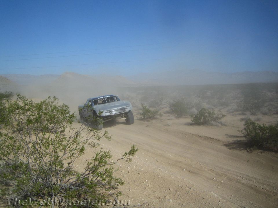 Silver trophy-style race truck airborne over a dusty desert road