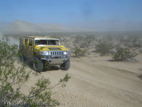 1990 Ford Bronco - yellow Hummer H3 with a spare tire navigates a sandy desert road trailing dust.