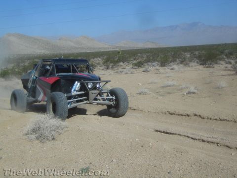 1990 Ford Bronco - black and red tube-frame off-road buggy with coilover shocks races along a flat desert trail.