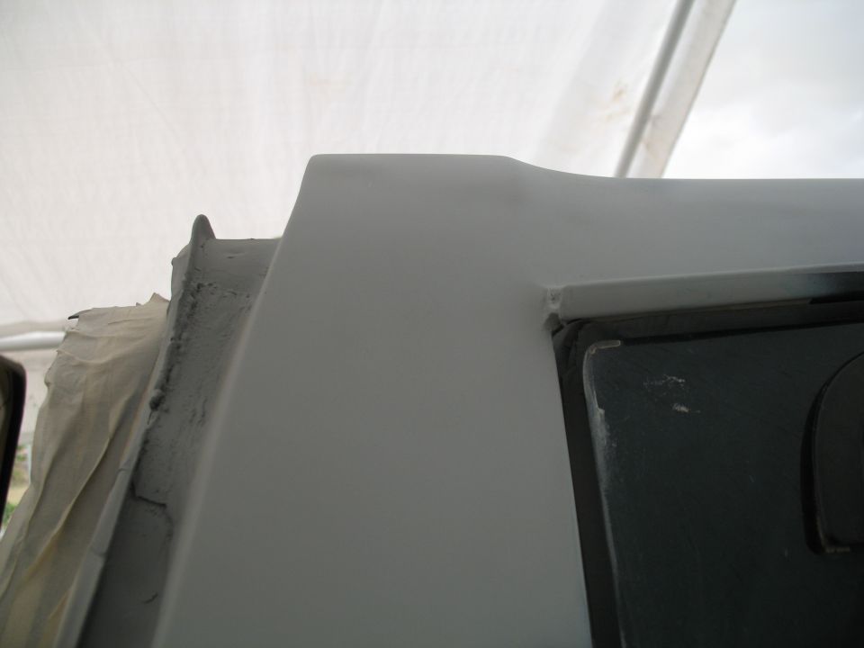 Close-up of a gray primered body panel corner on a vehicle under a tent