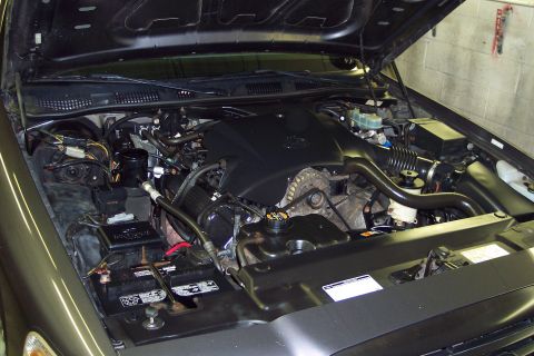 2001 Ford Crown Victoria - Open engine bay of a dark-colored Ford sedan showing the 4.6L V8 with its black plastic intake manifold cover, black valve cover with yello…