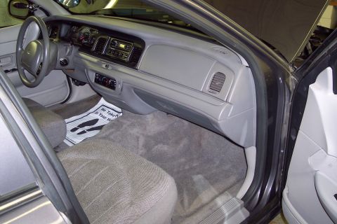 2001 Ford Crown Victoria - Interior view of a gray Ford sedan shot through the open passenger door, showing the dashboard, glovebox, front bench seat in gray cloth, a…