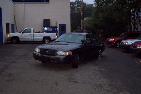 2001 Ford Crown Victoria - A black 2001 Ford Crown Victoria is parked in front of a building, with other vehicles visible in the background.