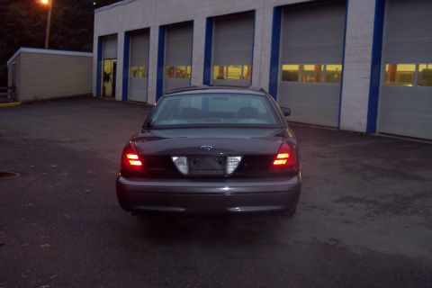 2001 Ford Crown Victoria - The rear of a 2001 Ford Crown Victoria is shown parked in front of a commercial building with garage doors.