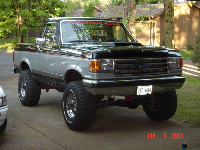 Lifted gray and black Ford pickup on large mud tires in a driveway, dated June 4 2003