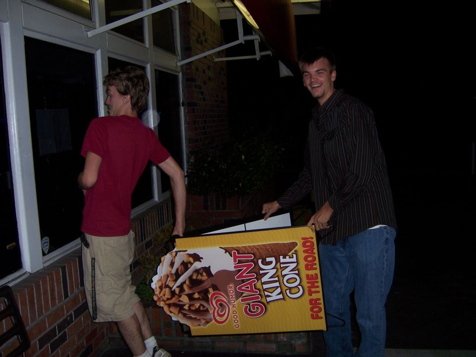 Two guys carrying a large sign for a Giant King Cone ice cream