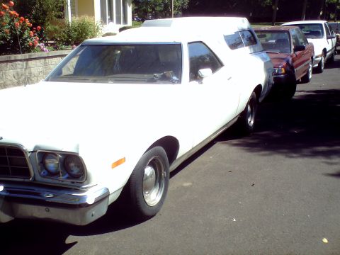 1973 Ford Ranchero - A white utility vehicle with a camper shell is parked on a street, with other vehicles behind it.