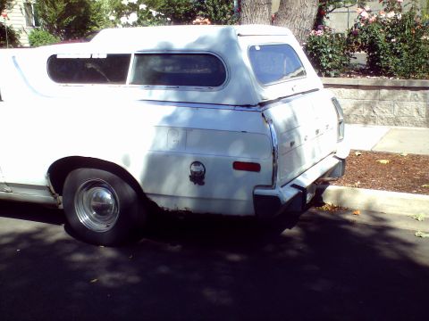1973 Ford Ranchero - Rear view of a 1973 Ford Ranchero pickup with a camper shell, displaying rust near the wheel well.