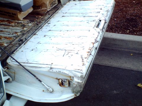 1973 Ford Ranchero - The rear tailgate of a white pickup truck shows significant wear and rust, with items in the bed behind it.