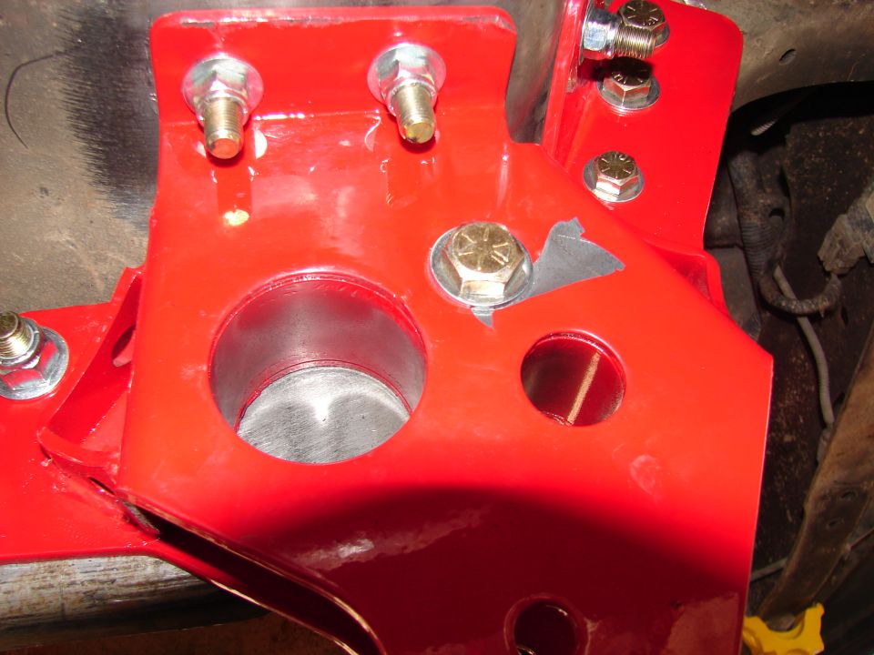 Red metal suspension component with visible bolts and circular openings