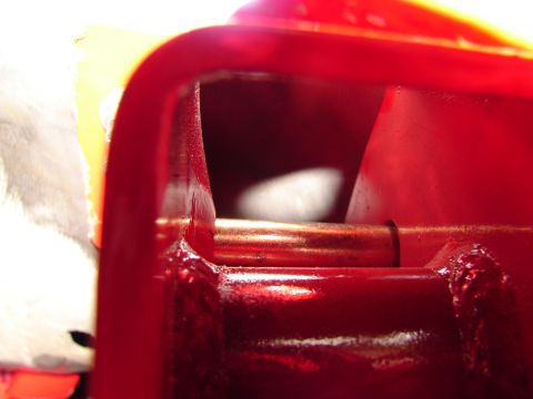 1996 Ford Bronco - Red metal part with a copper rod visible, likely from a vehicle's suspension or frame.
