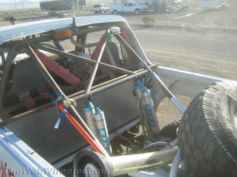 1990 Ford Bronco - open rear bed of an off-road race truck reveals a roll cage, blue bypass shocks and a mounted spare tire.