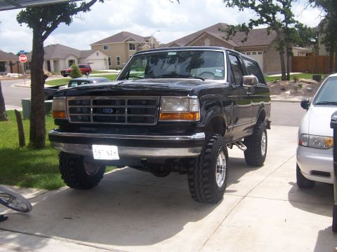 1993 Ford Bronco - This black 1993 Ford Bronco features a lifted suspension and chrome wheels, parked in a suburban driveway.