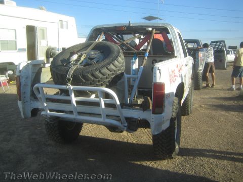 1990 Ford Bronco - white off-road truck shows its rear bumper and two bed-mounted spare tires while parked at a desert pit.