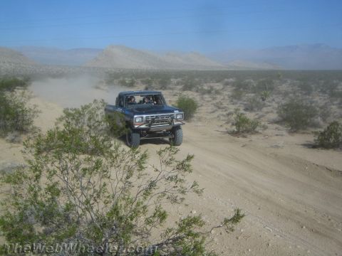 1990 Ford Bronco - blue lifted older Ford pickup with a tube bumper drives along a sandy desert trail dotted with brush.