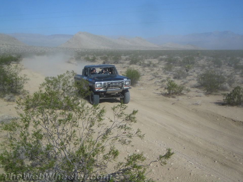 Blue lifted Ford pickup truck on a sandy desert trail among brush