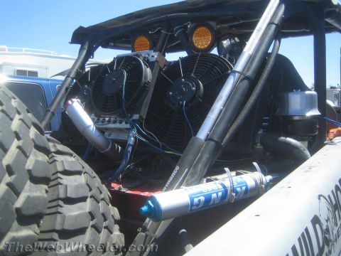 1990 Ford Bronco - Engine bay detail of an off-road race vehicle with twin electric cooling fans, plumbing, and a blue-collared bypass shock.