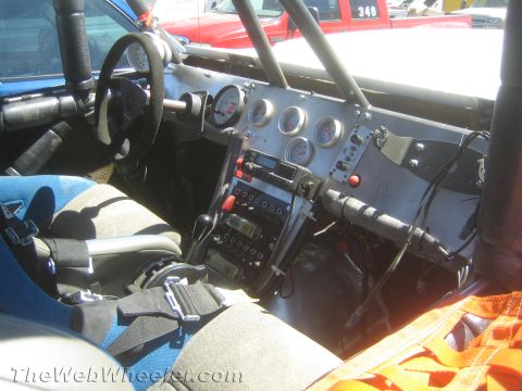 1990 Ford Bronco - Interior of a stripped off-road race truck showing a roll cage, custom gauge cluster, switch panels and racing bucket seats.