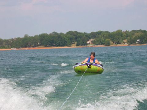 1985 Ford LTD Crown Victoria - person in a life vest holds on to a green and purple inflatable tube being towed across open lake water.