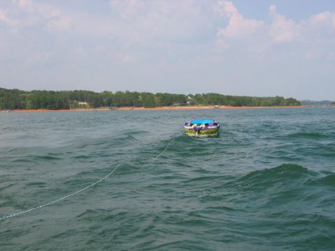 1985 Ford LTD Crown Victoria - A colorful purple, green, and blue inflatable towable tube floats on a choppy lake, connected by a tow rope, with a wooded shoreline in the…