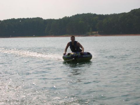 1985 Ford LTD Crown Victoria - A person enjoys a sunny day tubing on a large body of water with a treeline in the background.