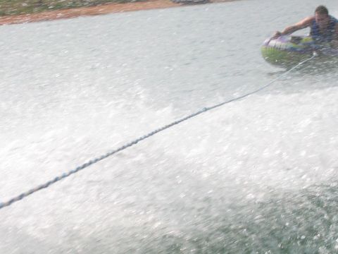 1985 Ford LTD Crown Victoria - A person enjoys tubing on a sunny day, pulled by a boat across the water.