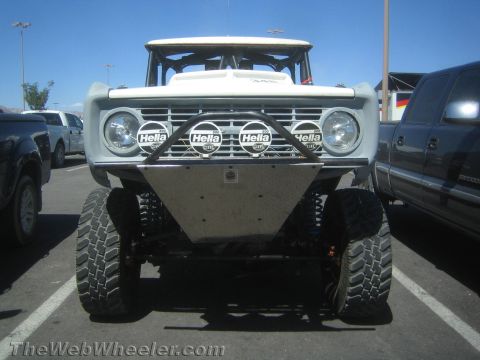 1990 Ford Bronco - Front view of a lifted white early Ford Bronco prerunner with a row of Hella driving lights and a steel skid plate.