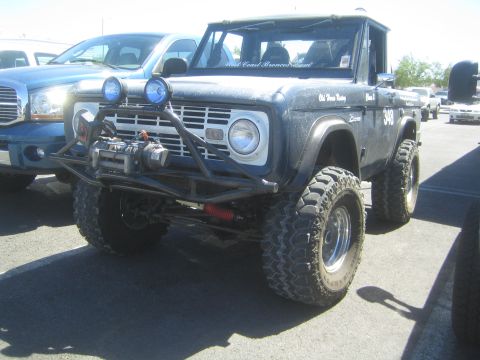 1990 Ford Bronco - lifted dark blue early Ford Bronco off-road truck with a front winch, tube bumper and round driving lights, parked in a lot.