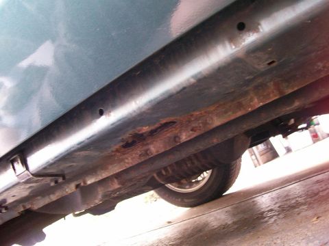 1995 Mercury Grand Marquis - The underside of a green vehicle shows significant rust damage along the rocker panel and frame.