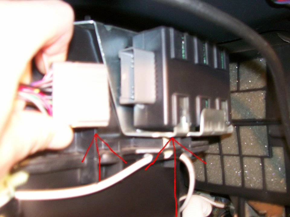 Close-up of a black electrical module with a white connector and red arrows pointing to mounting points