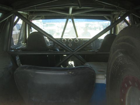 1990 Ford Bronco - View through the roll cage of an off-road race truck, looking forward past a bench seat toward the dash and a BFGoodrich tire.
