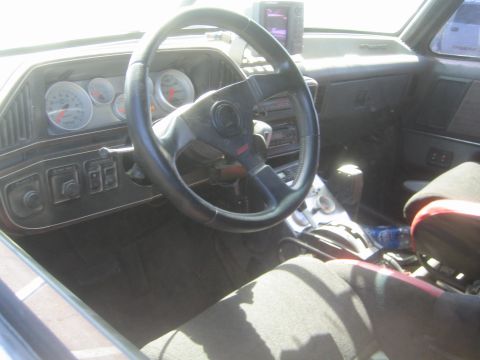 1990 Ford Bronco - Interior of a modified truck showing a leather-wrapped steering wheel, aftermarket gauge cluster and a floor-mounted shifter.