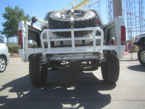 1990 Ford Bronco - Rear view of a lifted white off-road truck with a white tube bumper and a mounted spare tire, on a paved lot.
