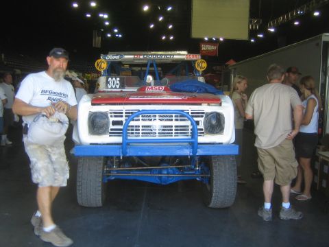 1990 Ford Bronco - red and white early Ford Bronco race truck numbered 305 with BFGoodrich and KC livery on display indoors as people gather.