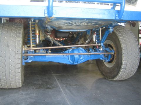 1990 Ford Bronco - Underside front view showing the blue painted front axle, shocks and tie rods of a Ford off-road truck.