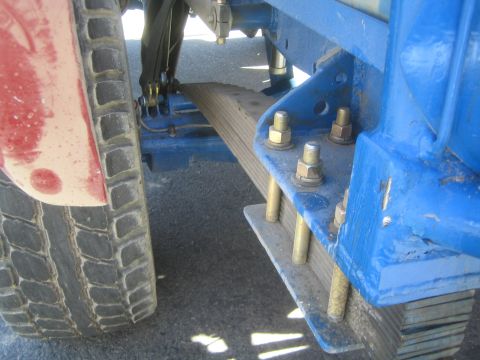 1990 Ford Bronco - Close-up of a leaf spring and blue painted mounting bracket bolted to the frame of an off-road truck.