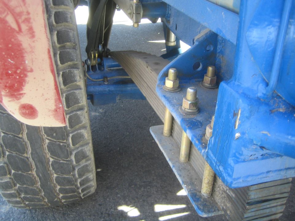 Close-up of leaf spring and blue mount bolted to frame on an off-road truck
