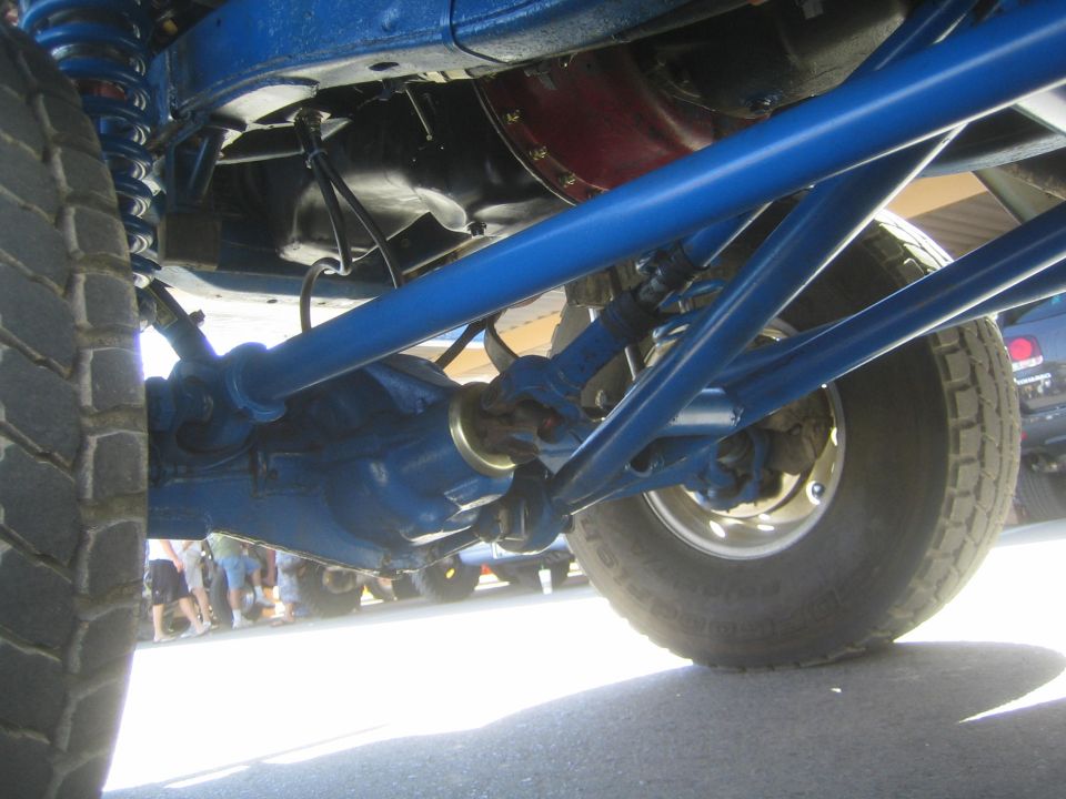 Underside view of off-road truck showing blue rear axle, driveshaft and coil springs
