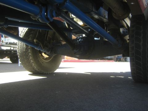 1990 Ford Bronco - Low ground-level view of the blue painted chassis links and suspension of an off-road truck on pavement.