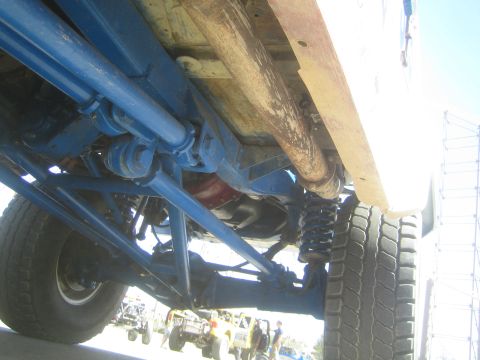1990 Ford Bronco - Underside view of an off-road truck showing blue suspension links, coil springs, driveshaft and rear tire.