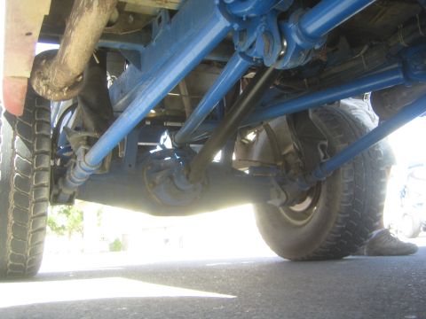 1990 Ford Bronco - Underside view of an off-road truck showing blue painted suspension arms, axle joints and tires on pavement.