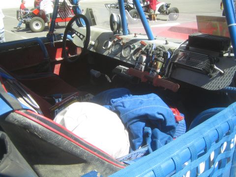 1990 Ford Bronco - Interior of an off-road race vehicle with a steering wheel, gauges, harnesses and a blue mesh window net.