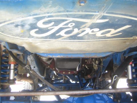 1990 Ford Bronco - Underside view showing a Ford-logo skid panel, leaf springs and blue painted frame of an off-road truck.