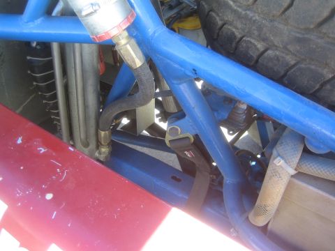 1990 Ford Bronco - Close-up of blue roll cage tubing, lines and fittings near a tire inside the chassis of an off-road truck.