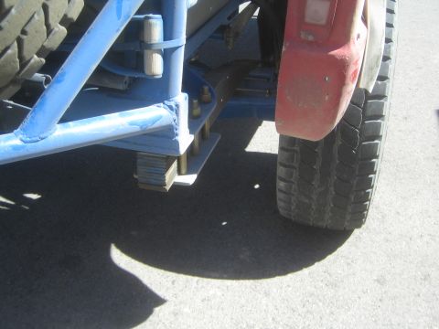 1990 Ford Bronco - Close-up of the blue frame, leaf-spring shackle mount and rear tire behind a red fender of an off-road truck.