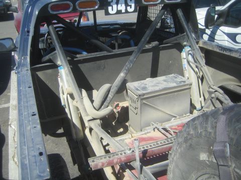 1990 Ford Bronco - Open rear bed of a prerunner pickup numbered 349 fitted with a roll cage, shocks, fuel cell and a metal ammo box.
