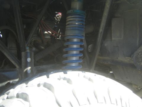 1990 Ford Bronco - Close-up of a blue coilover shock and spring mounted in the wheel well of an off-road truck above a dusty mud-terrain tire.