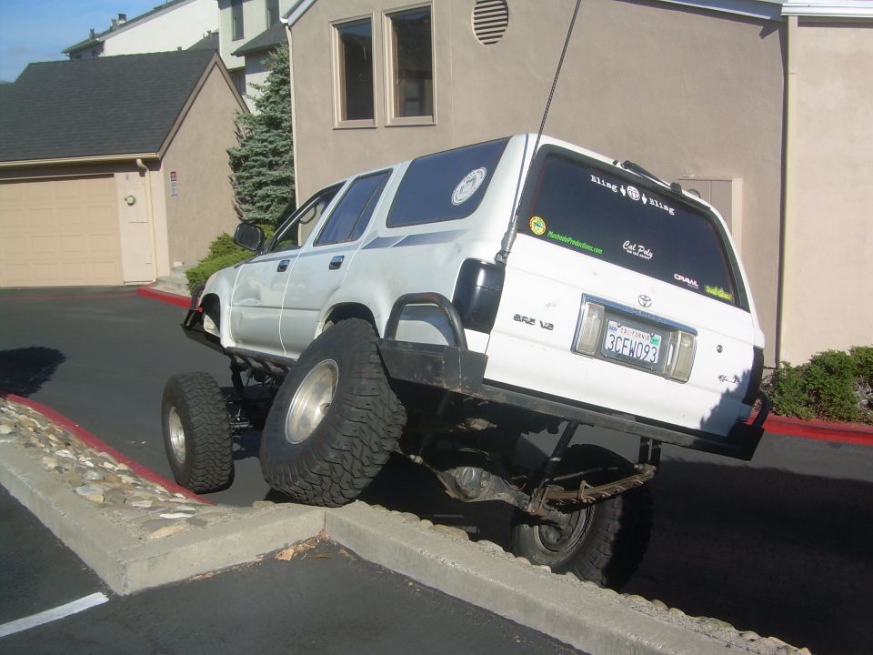 White lifted Toyota SUV flexing rear suspension with wheels up on a parking lot curb